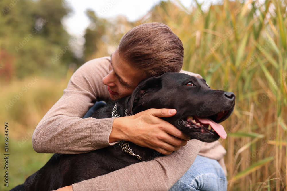 Smiling man hugging black cute dog outdoors Smiling man hugging black cute dog outdoors