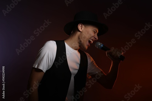 Talented young man singing on dark background with color light