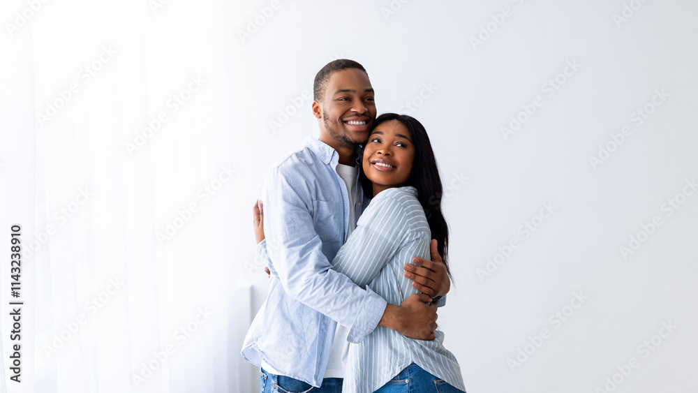 Happy young black spouses standing in their own house, hugging and smiling, being happy of buying own lodging. Cheerful african american family relocating to new property