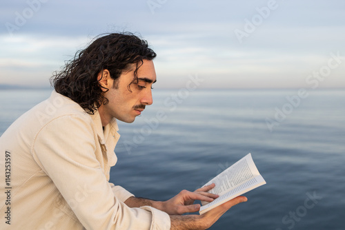 Man reading a book by the ocean at sunset with peaceful ambiance photo