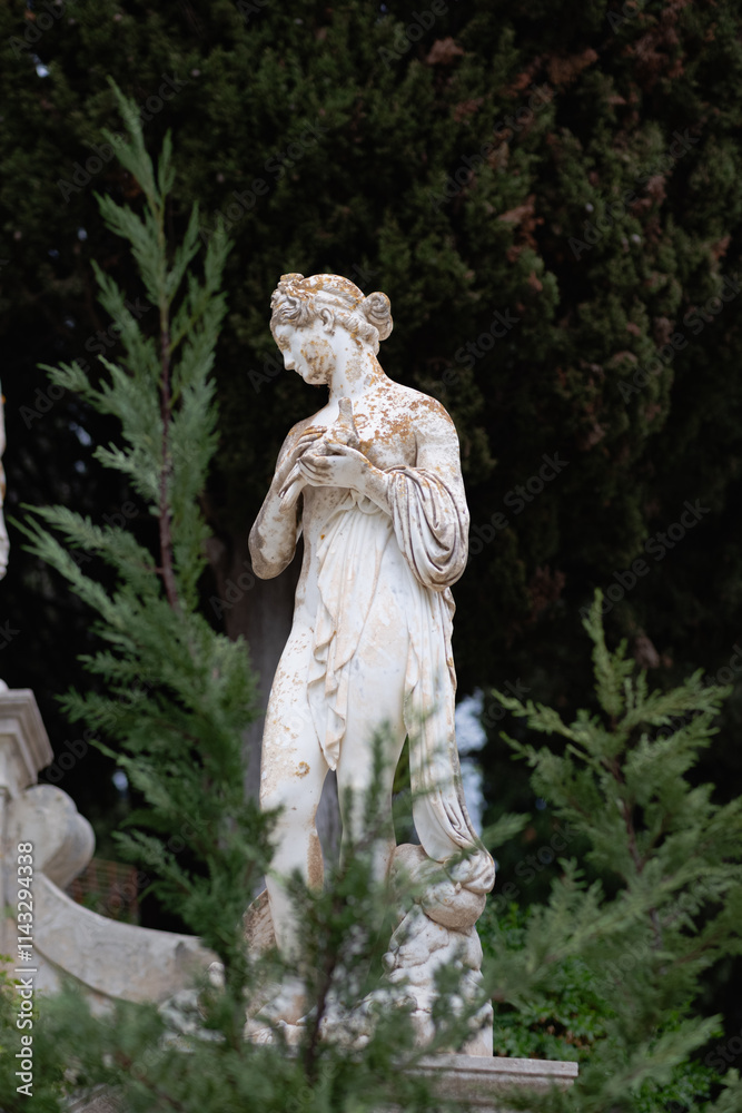 Obraz premium An antique statue made of white stone with a layer of old dirt stands among trees in a garden