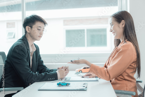 An Asian female employee of a car dealership hands keys to a new customer. Success in selling or leasing cars Happy young man receives new car keys