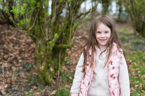 Little smiling girl in vest standing in spring park. Concept of active cheerful happy child