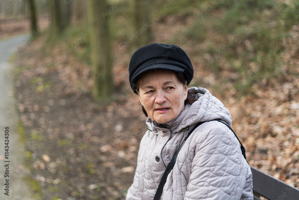 An elderly woman in a jacket and hat sits alone on a bench in a park. The concept of loneliness in old age An elderly woman in a jacket and hat sits alone on a bench in a park. The concept of loneliness in old age