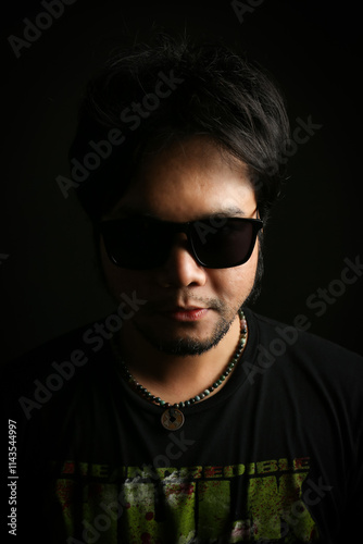 closeup of low key portrait of an Asian man wearing sun glasses on black background