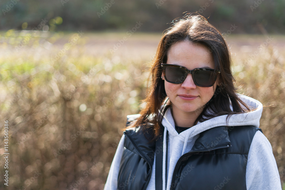 Cute smiling positive girl in sunglasses and vest standing outdoors in spring. Healthy active person concept Cute smiling positive girl in sunglasses and vest standing outdoors in spring. Healthy active person concept