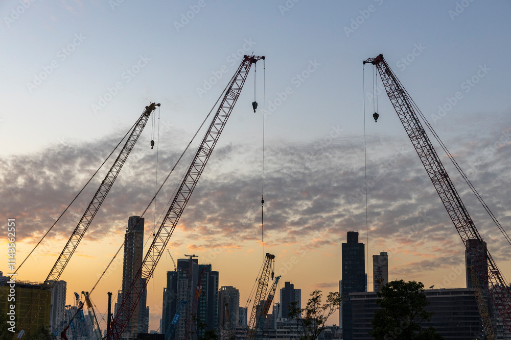 Dec 16 2024,Hong Kong.A series of construction cranes rise against a colorful sunset, casting long shadows over a busy construction site Dec 16 2024,Hong Kong.A series of construction cranes rise against a colorful sunset, casting long shadows over a busy construction site
