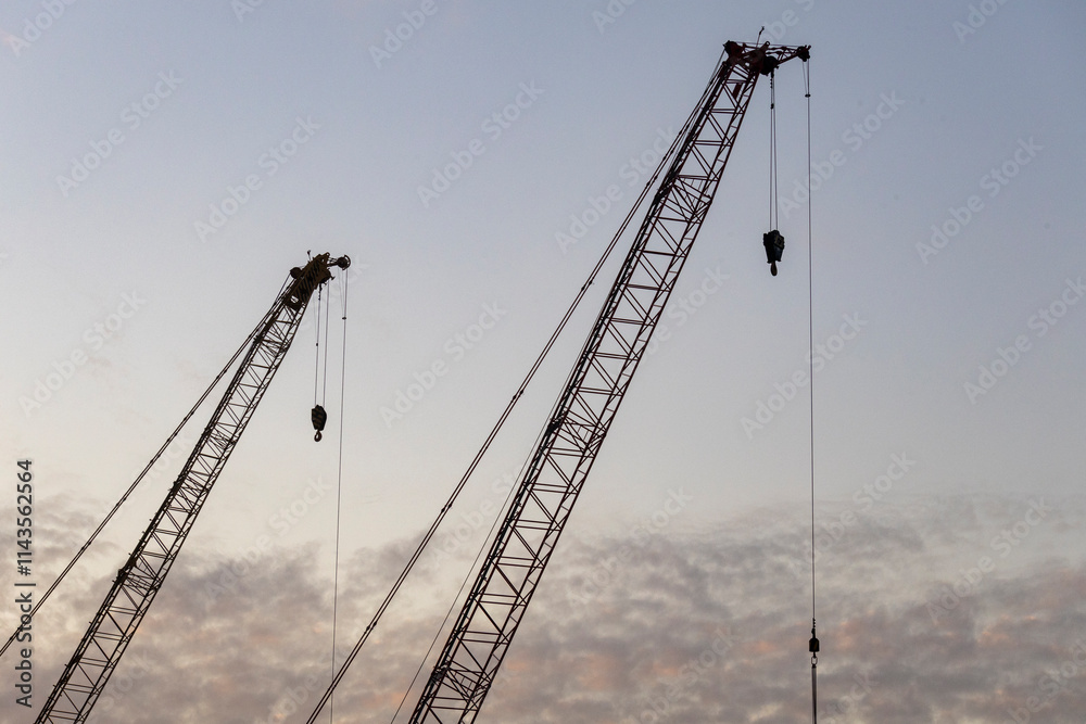 Dec 16 2024,Hong Kong.A series of construction cranes rise against a colorful sunset, casting long shadows over a busy construction site Dec 16 2024,Hong Kong.A series of construction cranes rise against a colorful sunset, casting long shadows over a busy construction site