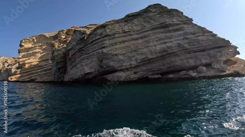 A magnificent rock formation juts out of the tranquil waters waves passing, revealing layered textures and captivating shapes that tell the story of time at Mina Al Fahal in Muscat, Oman.