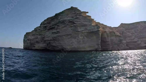 The rugged cliffs rise majestically from the deep blue waters, creating a stunning contrast with the clear sky, embodying the natural beauty at Mina Al Fahal in Muscat, Oman.