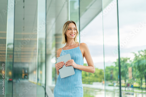 Beautiful Caucasian Woman in Blue Dress Holding Tablet Indoor a Modern Glass Office Building in the Business and Finance District, Looking Away Smiling Free Download Beautiful Caucasian Woman in Blue Dress Holding Tablet Indoor a Modern Glass Office Building in the Business and Finance District, Looking Away Smiling - GFXLoad