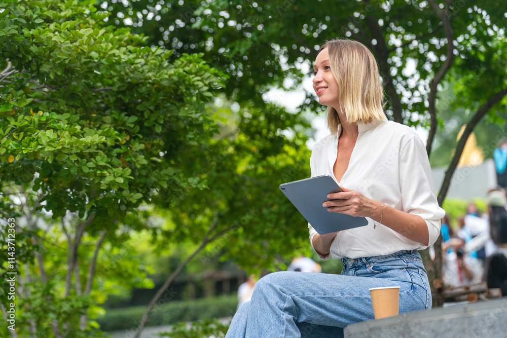 Obraz premium Caucasian Woman Sitting and Using Tablet While Having a Cup of Coffee Outdoor a Park
