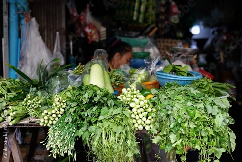 Thai woman selling assorted Asian green vegetables at a market stall at Soi 20, an open morning street market in Silom - Bang Rak, Bangkok, Thailand photo