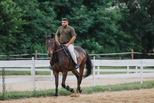 Man enjoying a horse ride in an outdoor equestrian arena with green trees in the background photo