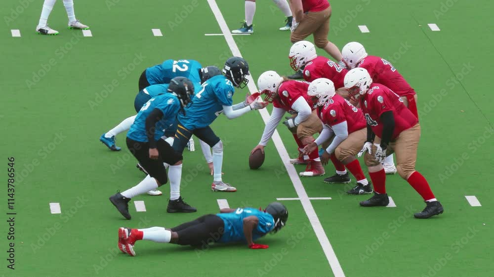 Two American Football Teams Stand Across From Each Other on the Line of Scrimmage as the Ball is Passed to Start the Game. Gridiron Players Stand and Defend Positions When the Ball is Played Two American Football Teams Stand Across From Each Other on the Line of Scrimmage as the Ball is Passed to Start the Game. Gridiron Players Stand and Defend Positions When the Ball is Played