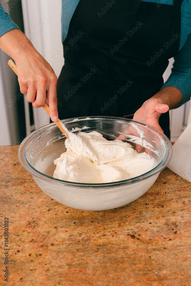 Baker in kitchen mixing vanilla frosting in bowl Baker in kitchen mixing vanilla frosting in bowl