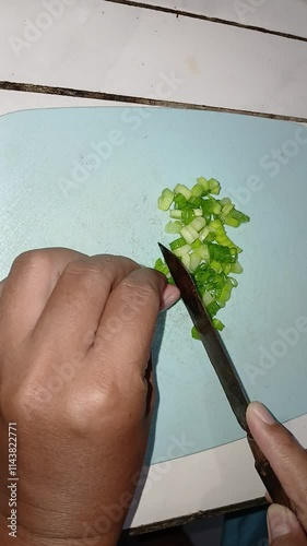 Portrait of a hand cutting spring onions using a knife with a plastic base or cutting board.