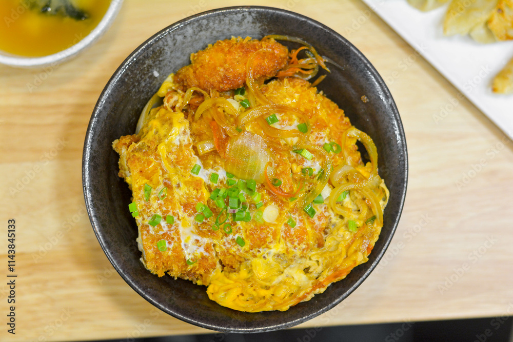 Japanese food concept. Chicken and egg rice bowl or Oyakodon in a black bowl with green onion topping. Japanese food concept. Chicken and egg rice bowl or Oyakodon in a black bowl with green onion topping.