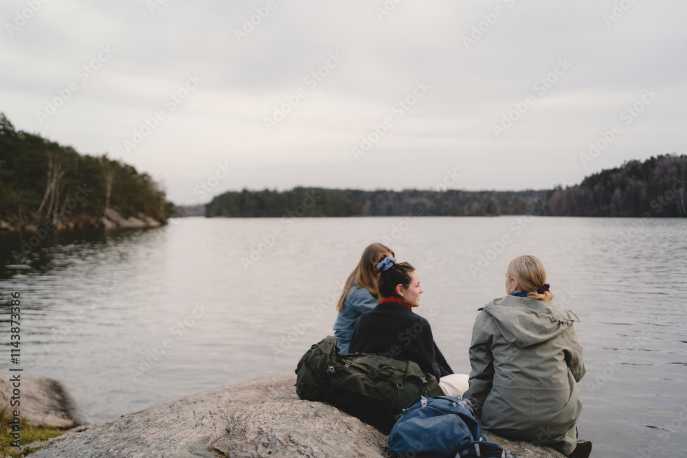 Rear view of female friends sitting at lakeshore Rear view of female friends sitting at lakeshore