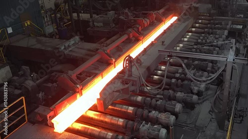 Witness the intense process of hot steel billets being transported on a conveyor in a steel mill. The glowing metal highlights the industrial operation. photo