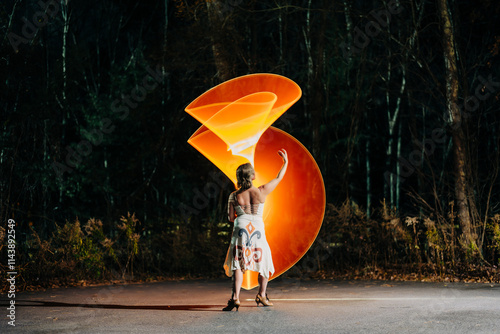 Woman posing at night with glowing orange spiral light art photo