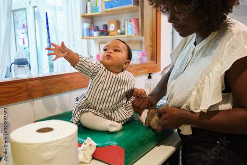 Mother dressing her baby girl on changing mat at home