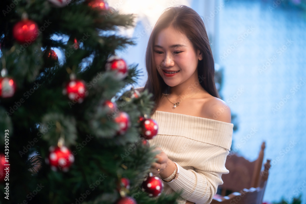 Portrait of beautiful happy Smiling asian woman relaxing sitting decorating to a Christmas tree at home in the living room indoors Decoration During Christmas x-mas and New Year holidays. Portrait of beautiful happy Smiling asian woman relaxing sitting decorating to a Christmas tree at home in the living room indoors Decoration During Christmas x-mas and New Year holidays.