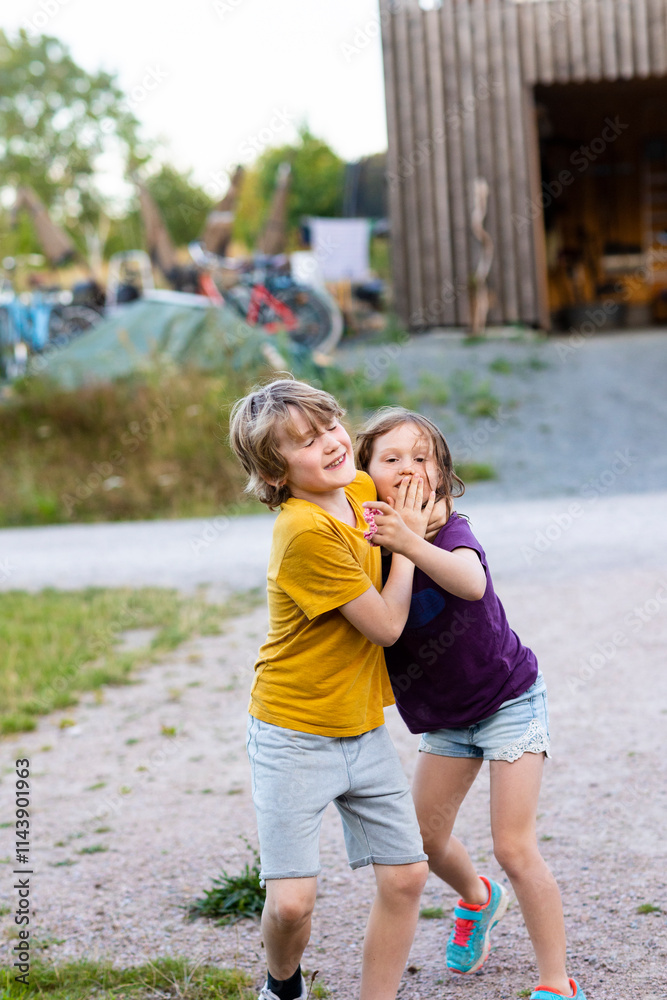 Playful brother covering sisters mouth while standing on dirt road Playful brother covering sisters mouth while standing on dirt road