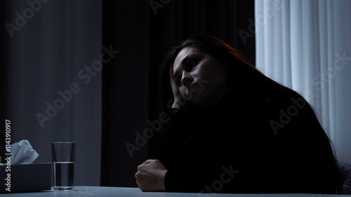 Silhouette of woman suffering mental health issues, sitting at the table, depressed expression, looks up thinking, melancholic face, side shot. photo