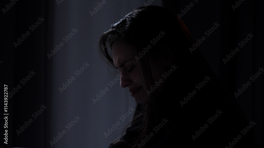 Silhouette of woman with mental health issues, sitting on the sofa, depressed expression, crying upset disappointed face looks down, close shot. Silhouette of woman with mental health issues, sitting on the sofa, depressed expression, crying upset disappointed face looks down, close shot.