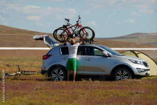 Autotourism. Wild family tourism to Koyash Lake. A man removes from the roof of the car bicycles. Near tourist tent. photo