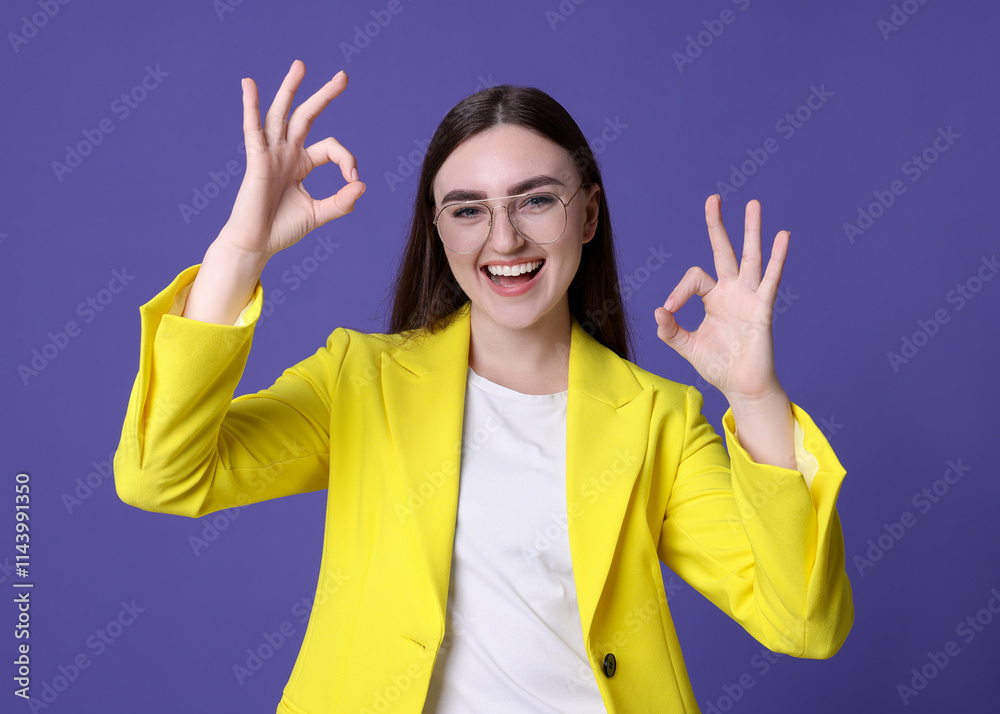Happy young woman showing OK gesture on violet background Happy young woman showing OK gesture on violet background