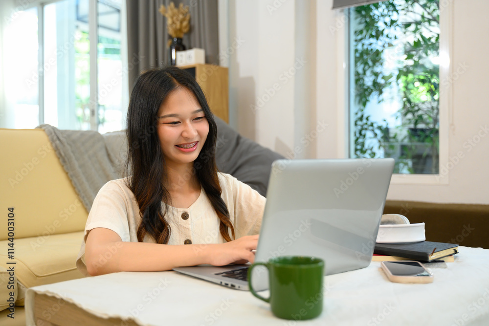 Cheerful young woman freelancer working with laptop on table in living room Cheerful young woman freelancer working with laptop on table in living room