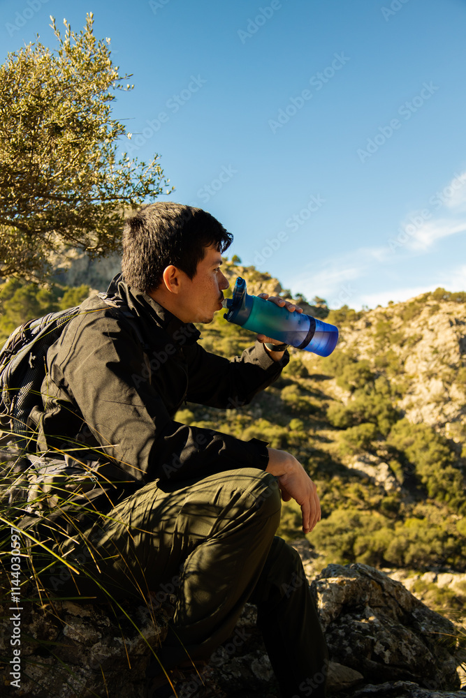 Vertical image of young hiker on top of a mountain sitting drinking water from a bottle on a sunny day Vertical image of young hiker on top of a mountain sitting drinking water from a bottle on a sunny day