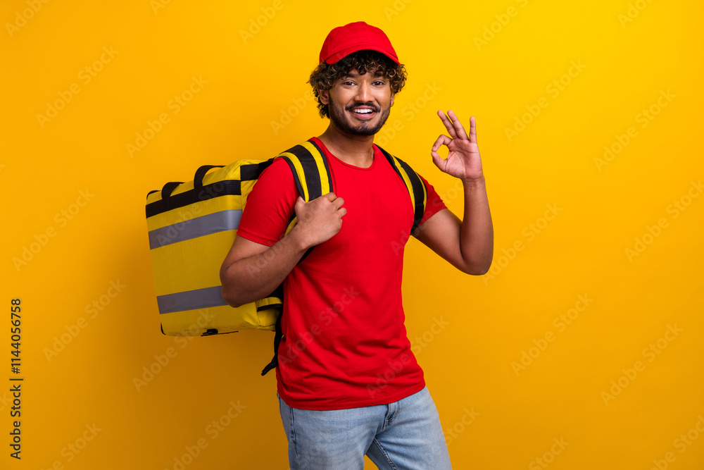 Portrait of a cheerful deliveryman in a red t-shirt and cap with a yellow backpack against a vibrant yellow background Portrait of a cheerful deliveryman in a red t-shirt and cap with a yellow backpack against a vibrant yellow background