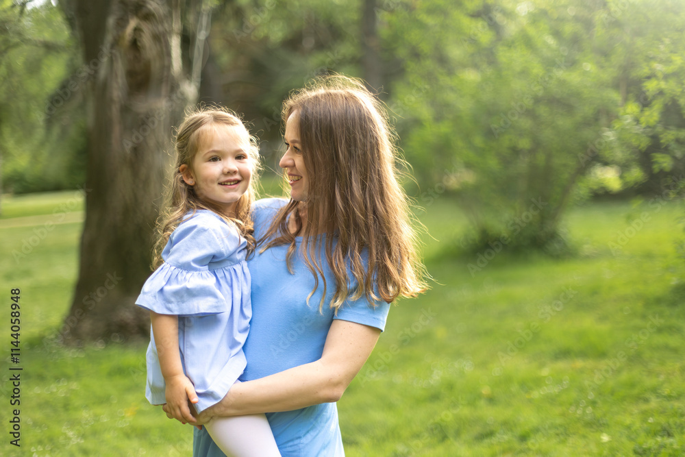 Mother holding smiling daughter in green park Mother holding smiling daughter in green park