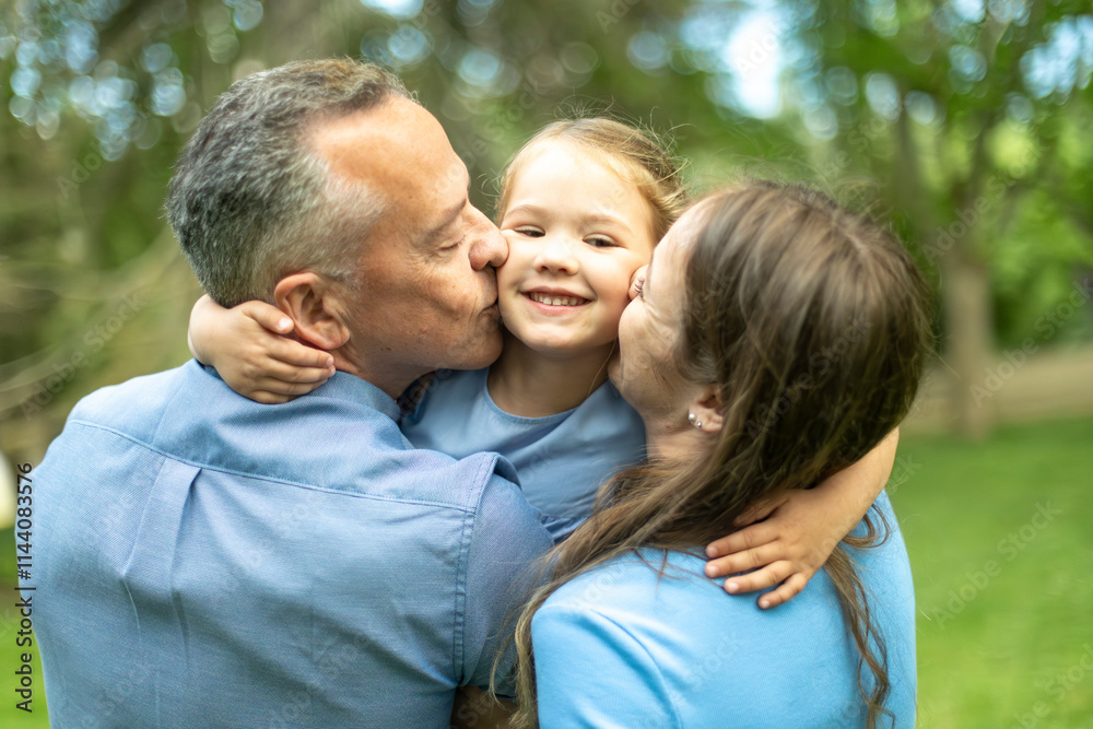 Parents kissing daughter on the cheek in a park Parents kissing daughter on the cheek in a park