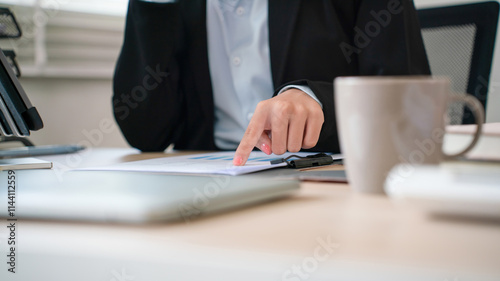 Businesswoman sitting at desk on couch in workplace or at home working on laptop and analyzing data on charts and graphs and writing on papers to make business plan and strategies for company, 