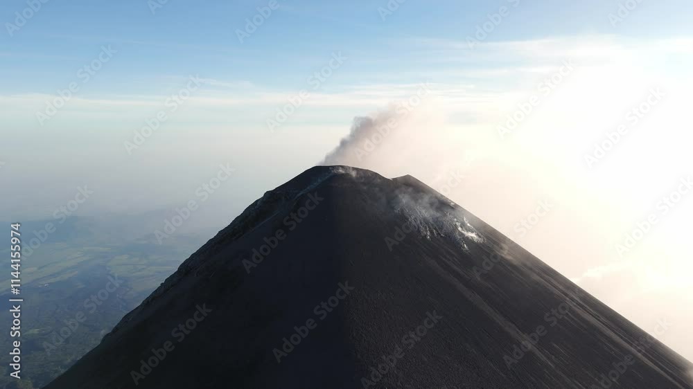Volcan de Fuego peak smitting a faint plume of smoke, showcasing natural active under a clear blue sky and serene backdrop
