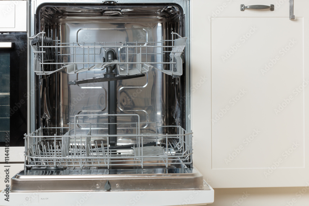 Built-in empty dishwasher with its door open. Modern technologies in the home kitchen with minimalistic white cabinetry. Simplifying daily housework. Built-in empty dishwasher with its door open. Modern technologies in the home kitchen with minimalistic white cabinetry. Simplifying daily housework.