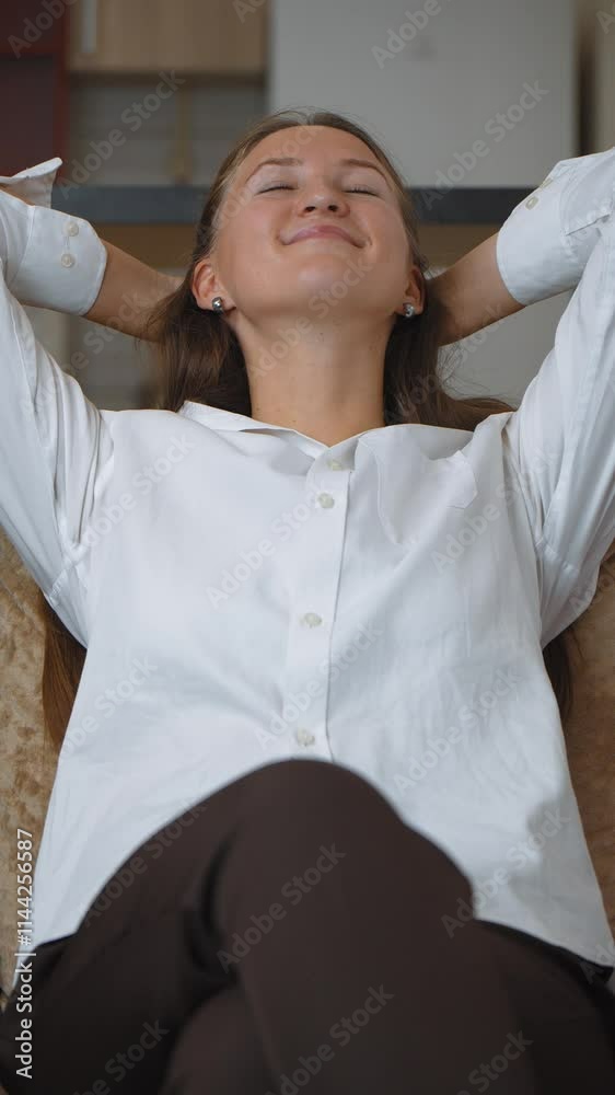 Businesswoman sits comfortably in her office, hands resting behind her head. Enjoying moment of relaxation, she embodies sense of calm and satisfaction amidst her work environment. vertical video