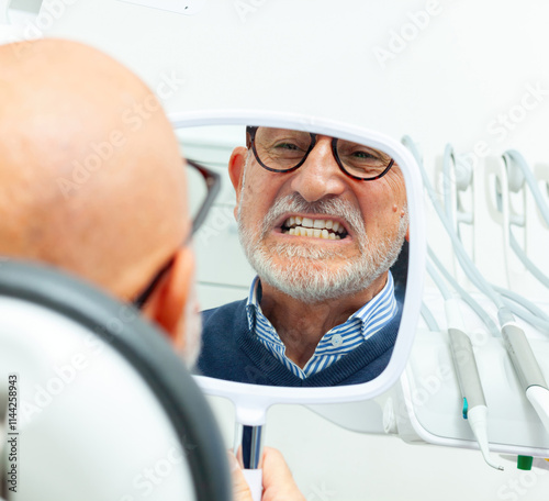 Senior man checking teeth in dental clinic mirror