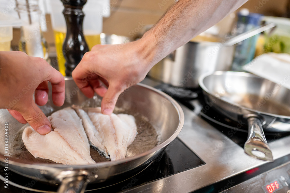 Two hands carefully place fish fillets in a hot frying pan, cooking in a bustling kitchen. The scene captures the culinary process, showcasing fresh ingredients and a vibrant kitchen atmosphere. Two hands carefully place fish fillets in a hot frying pan, cooking in a bustling kitchen. The scene captures the culinary process, showcasing fresh ingredients and a vibrant kitchen atmosphere.