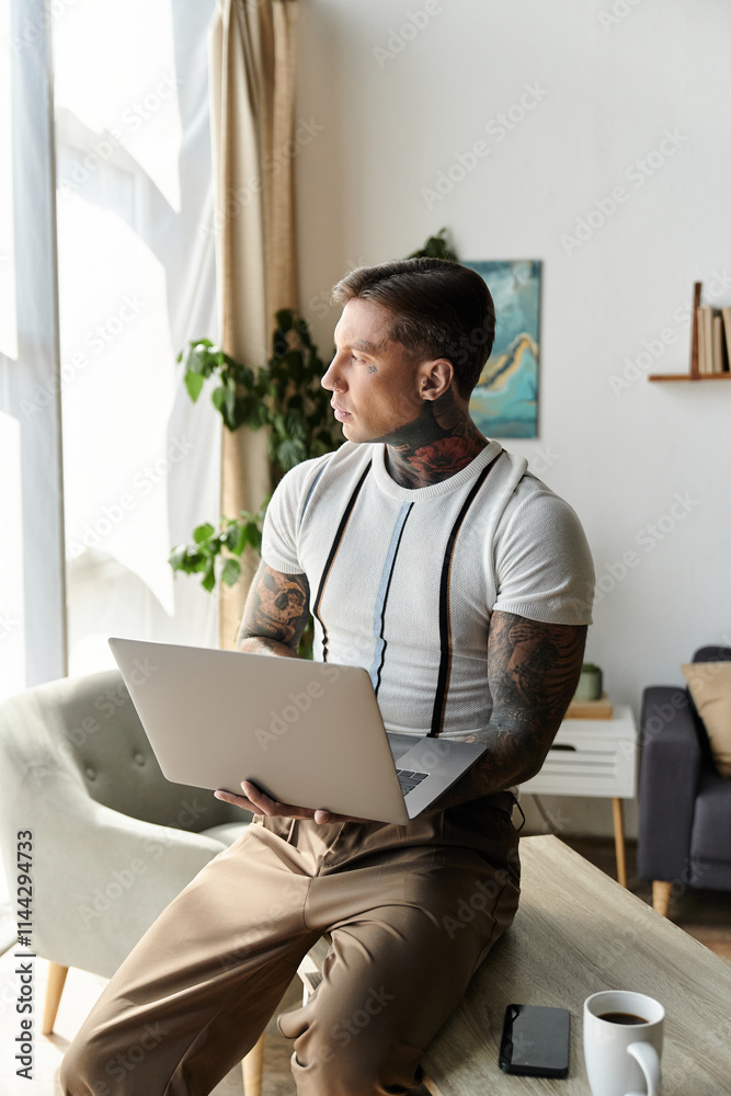 Young handsome man with tattoos is focused on his laptop in a stylish room. Young handsome man with tattoos is focused on his laptop in a stylish room.
