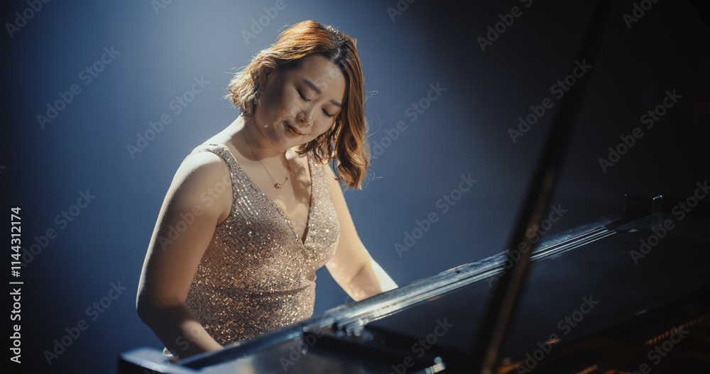 Fototapeta premium Portrait of a Talented Asian Pianist Captivating Audience with a Masterful Performance on a Grand Piano. Under Soft Stage Lights, Her Fingers Move Across the Keys, Creating Beautiful Classical Music
