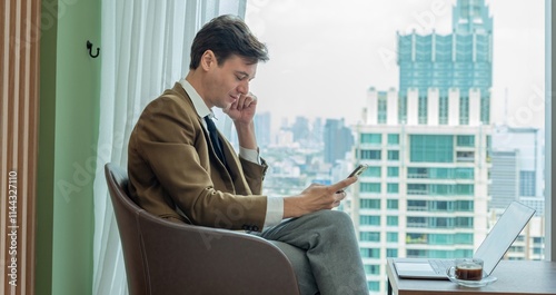 A man in a suit is sitting in a chair and looking at his phone.