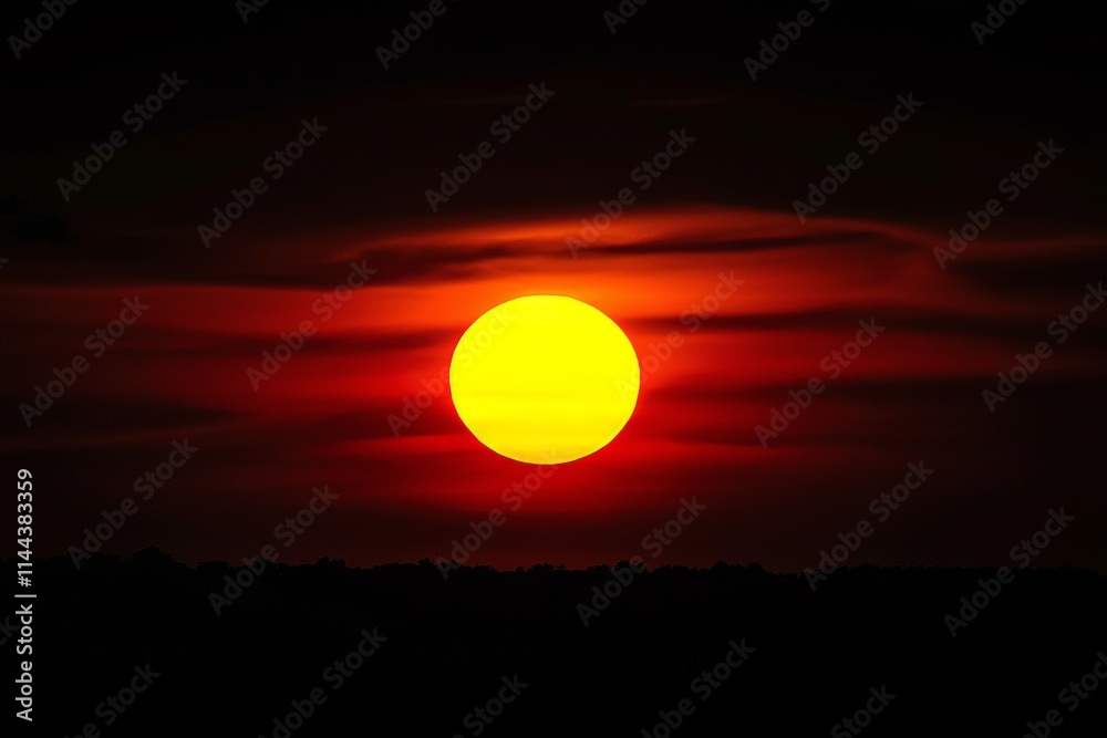 At sunset, a huge orange sun peeks through clouds on a black background. At sunset, a huge orange sun peeks through clouds on a black background.