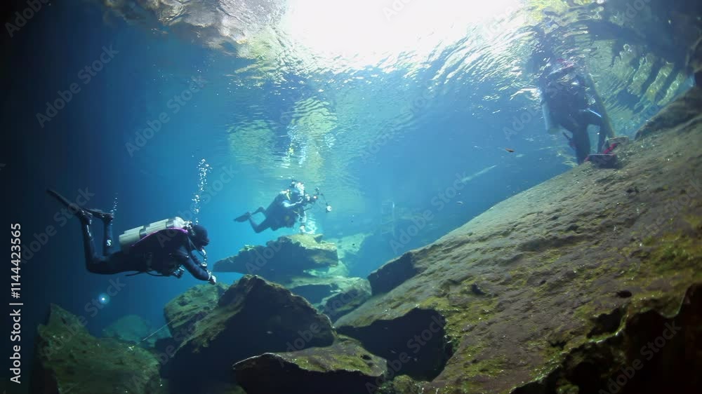 A group of people are scuba diving in a cave. The cave is filled with water and rocks
