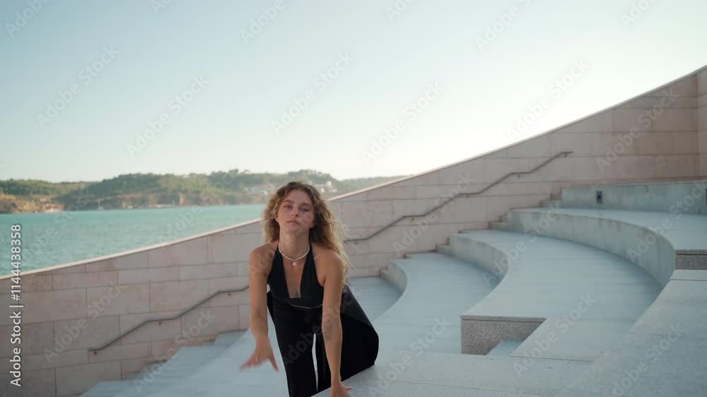 Sensuous woman in black dress moves gracefully on steps during sunny day, her movements elegant and fluid, creating a striking and captivating scene Sensuous woman in black dress moves gracefully on steps during sunny day, her movements elegant and fluid, creating a striking and captivating scene