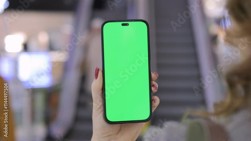 Wallpaper Mural A woman is holding a smartphone featuring a green screen in a modern, urban setting Torontodigital.ca